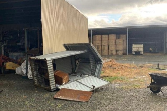 an image of a corrugated iron toilet building flipped over after a storm