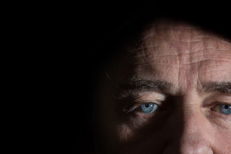 Close up image of a man's face, who stares at the camera with a blank expression.