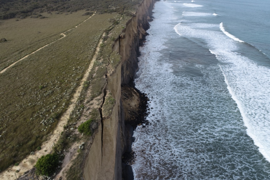 An aerial shot of cliffs over the ocean showing a large crack in the cliff face. 