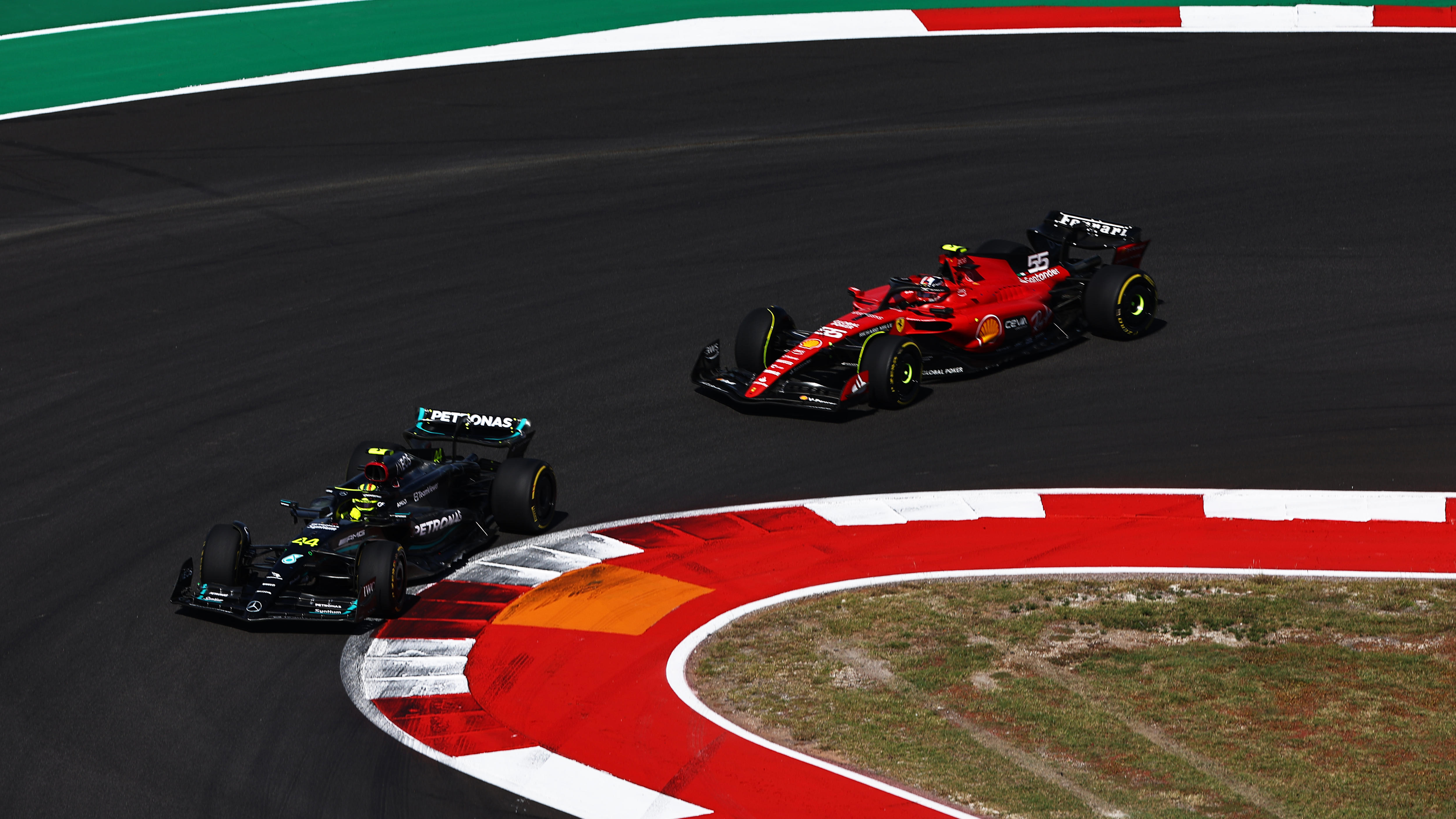 A black F1 car leads a red F1 car through a hair-pin turn
