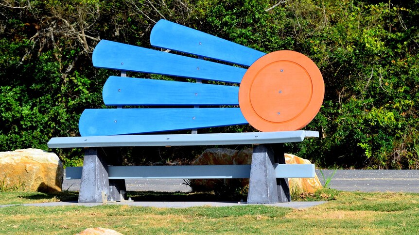Plywood seatback, with orange circle depicting the sun and four blue rays radiating out. Designed by Sarah Anderson.