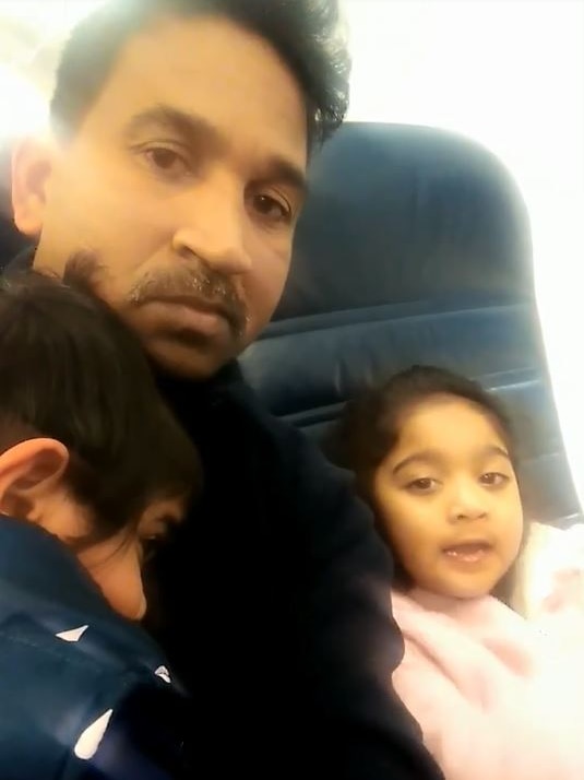 A man holding a sleeping child and a young girl look at the camera.