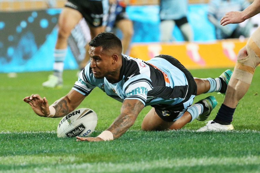 Ben Barba grimaces as he slides down to score a try during an NRL game. He is in a Cronulla Sharks uniform