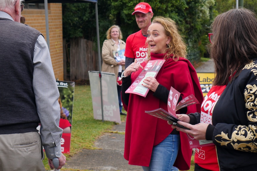 A woman in a red poncho with an animated look on her face points to a flyer she is holding