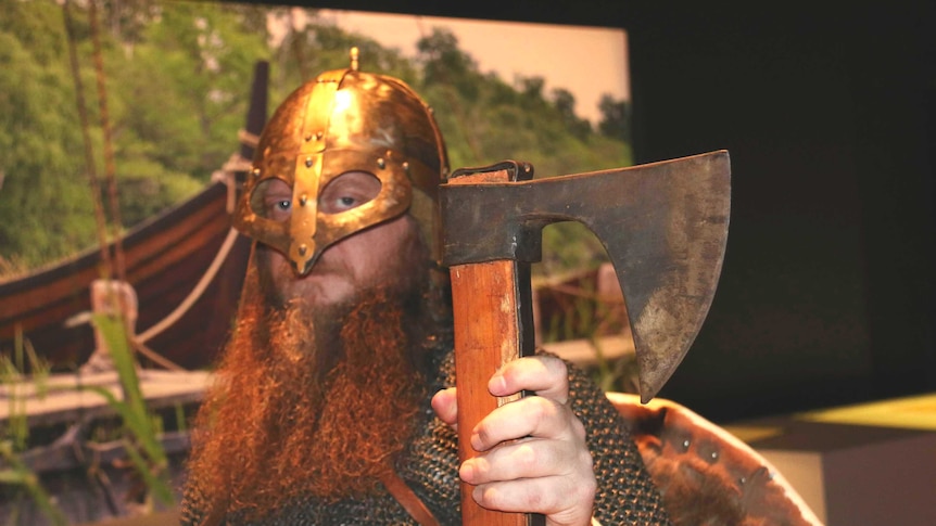 A man dressed as a viking, wearing a helmet and holding an axe.