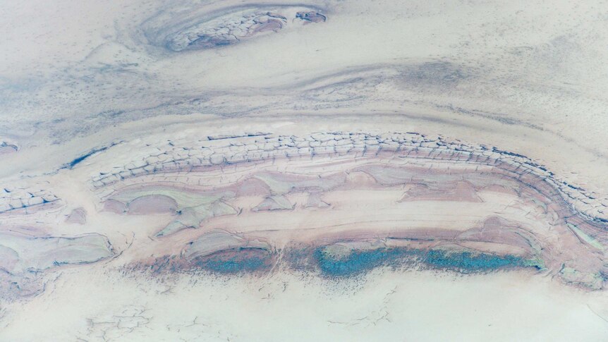 A pink dusty shot of a salt plain with strips of green.