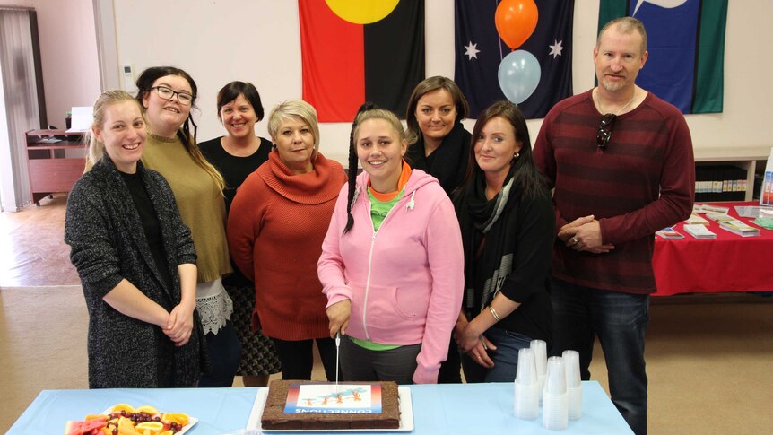 A group of peer support workers and representatives from mental health organisations gather to cut cake