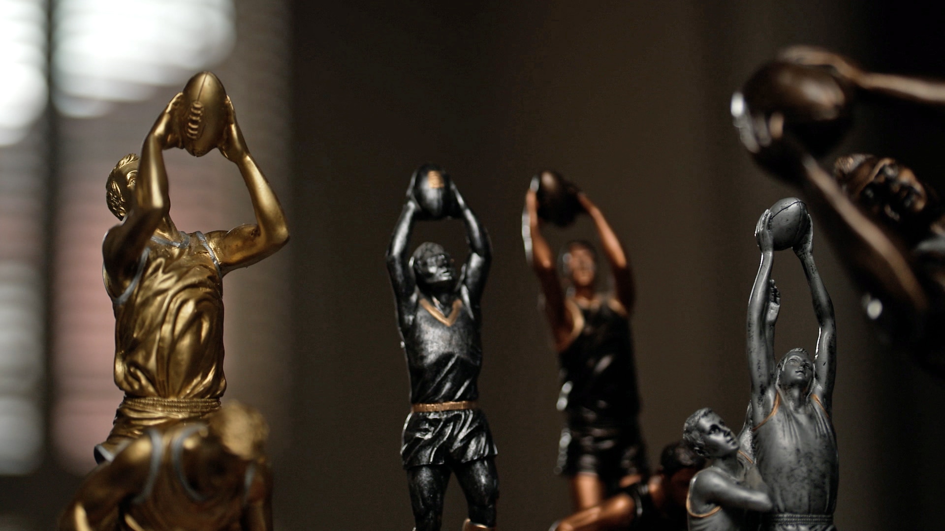 Five close-ups of AFL trophies. They are silver, bronze, and gold.