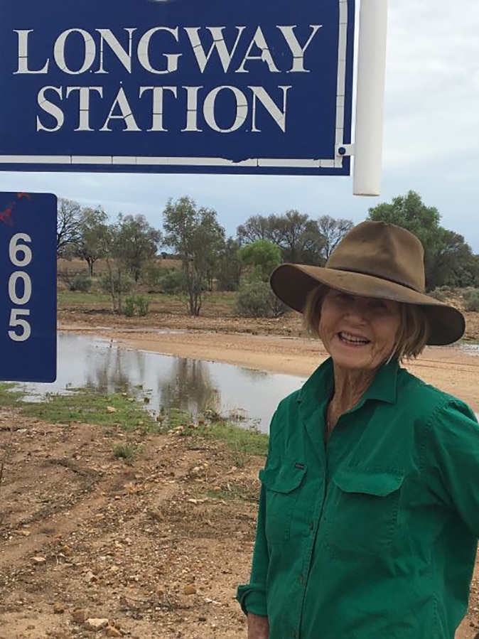 Rosemary Champion smiles as she stands beside Longway station sign after rain.