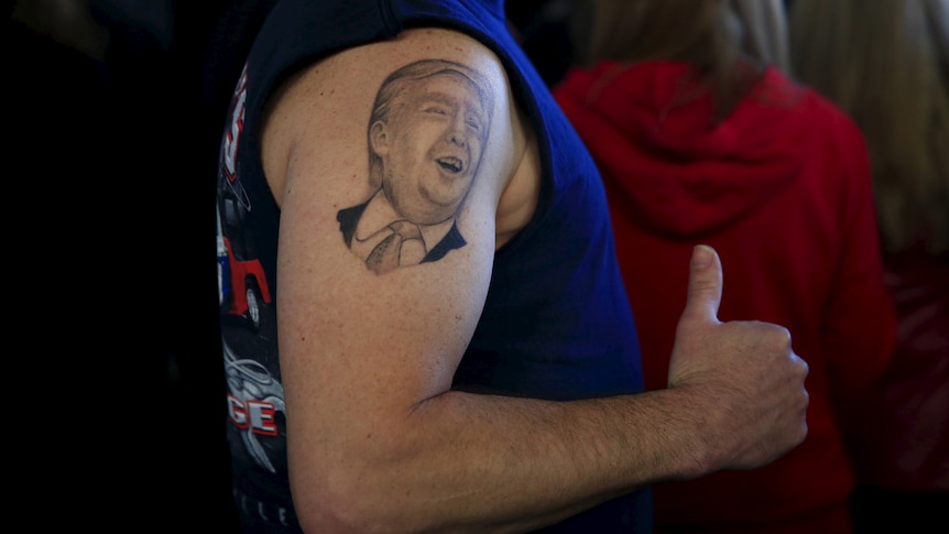 On a man's upper arm, a black and white tattoo of Trump's face can be seen. 
