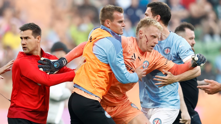 A bleeding Tom Glover of Melbourne City is escorted from the pitch by team mates after fans stormed the pitch