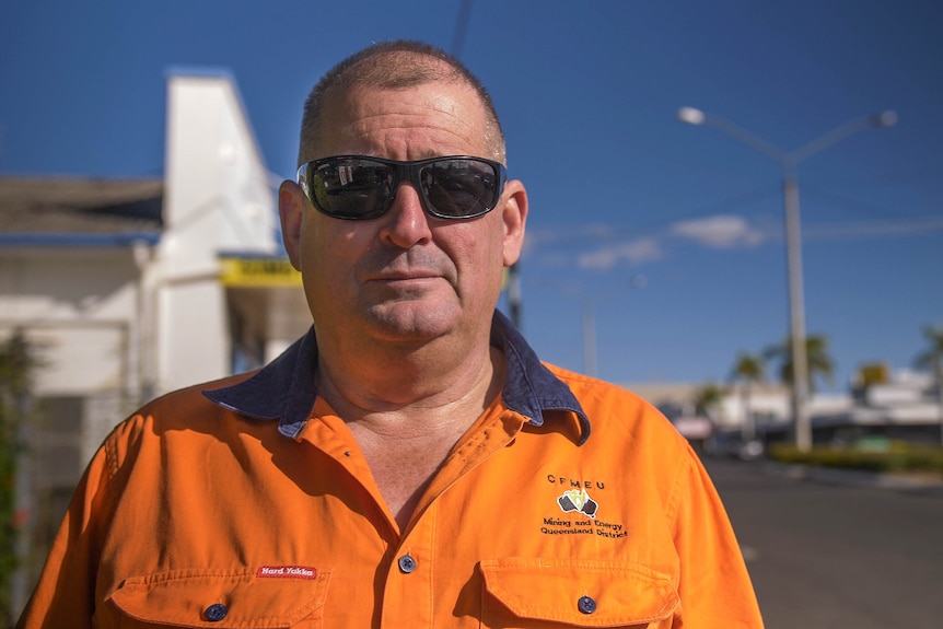 Un homme en orange haute visibilité, avec des lunettes de soleil foncées, se tient dans la rue principale de Clermont.