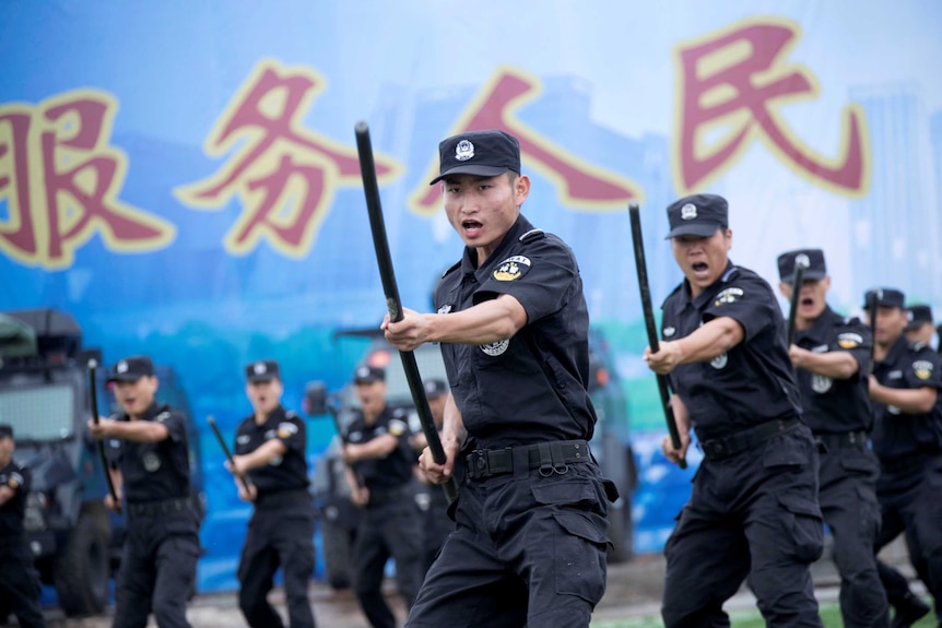 Chinese special force police officers perform a striking motion with a baton at a security oath-taking rally.