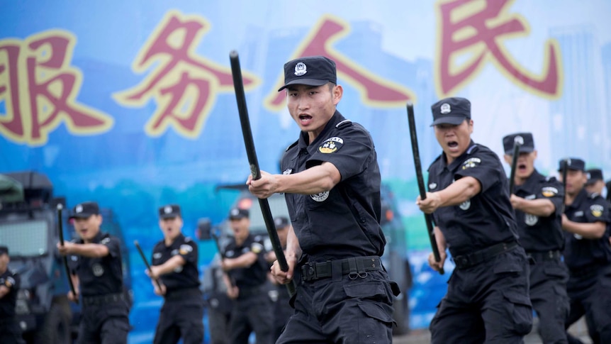 Chinese special force police officers perform a striking motion with a baton at a security oath-taking rally.