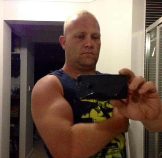 A man in a singlet taking a selfie in the mirror