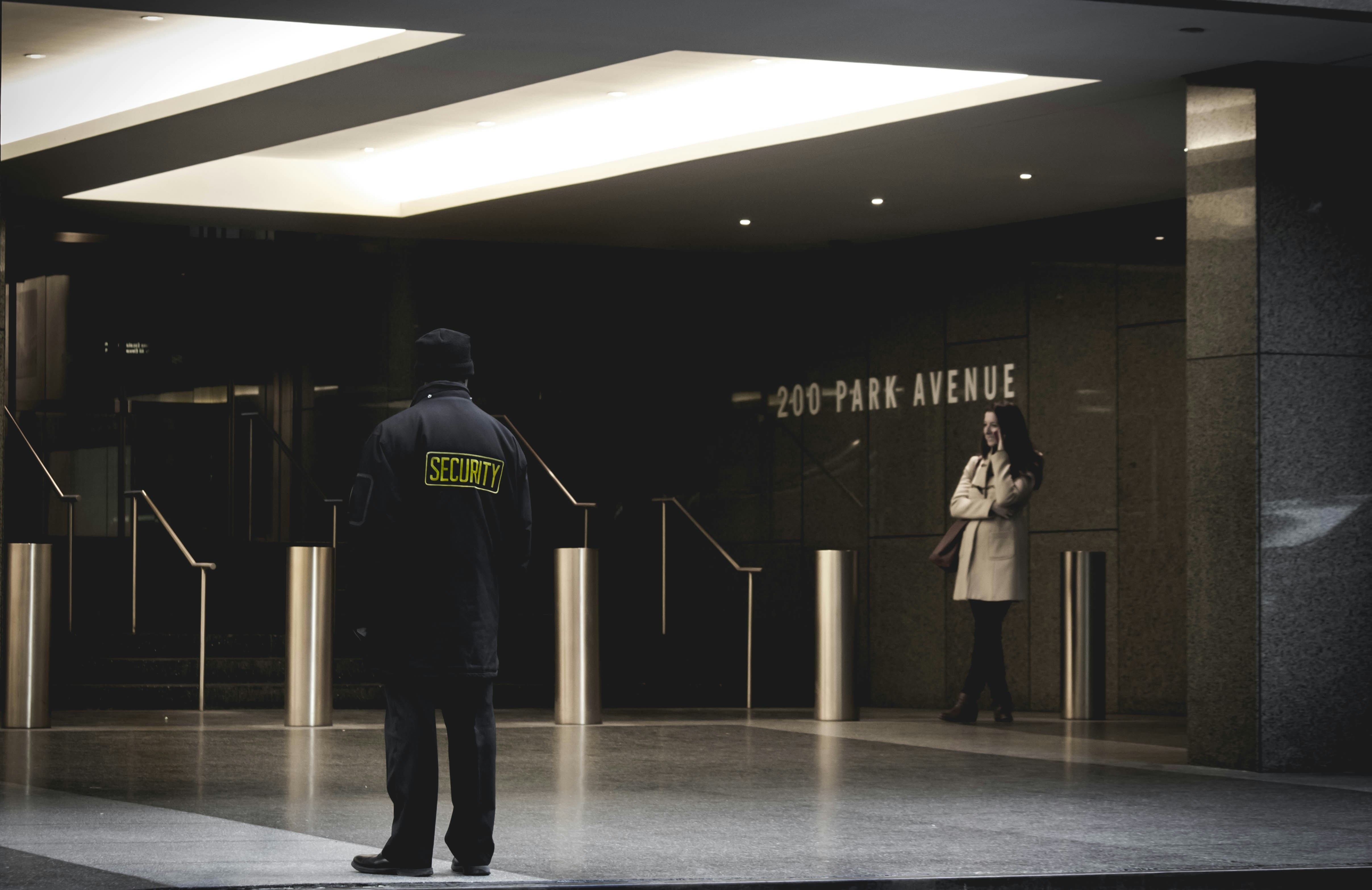 Back of security guard in jacket and beanie outdoors, woman to side
