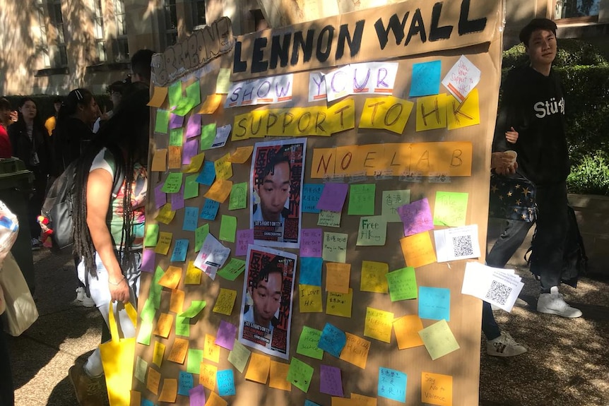 A board marked Lennon Wall stands against a tree with notes and photos pinned to it.