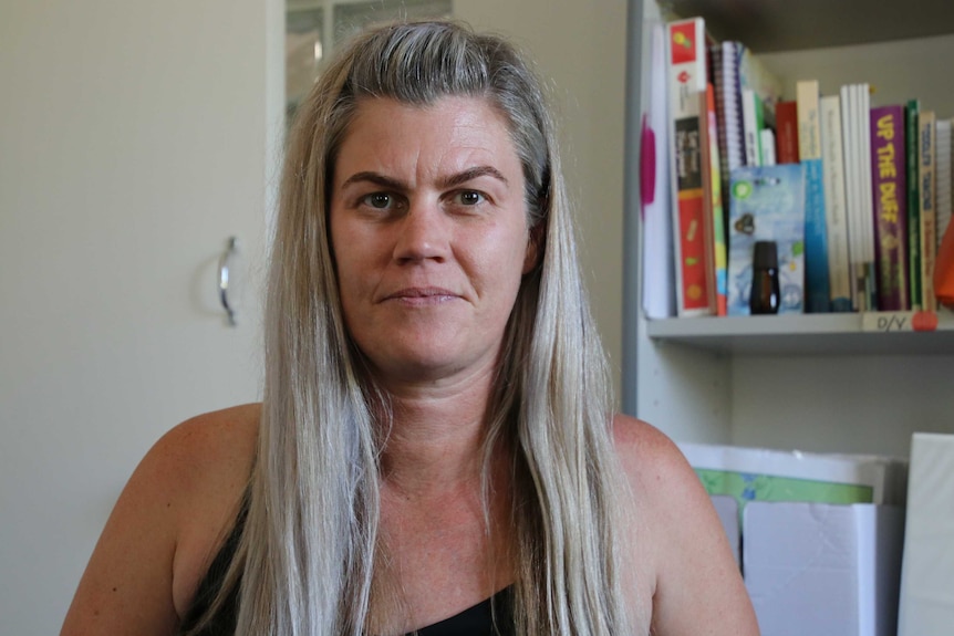 A photo of a woman with long hair standing in front of a bookshelf.