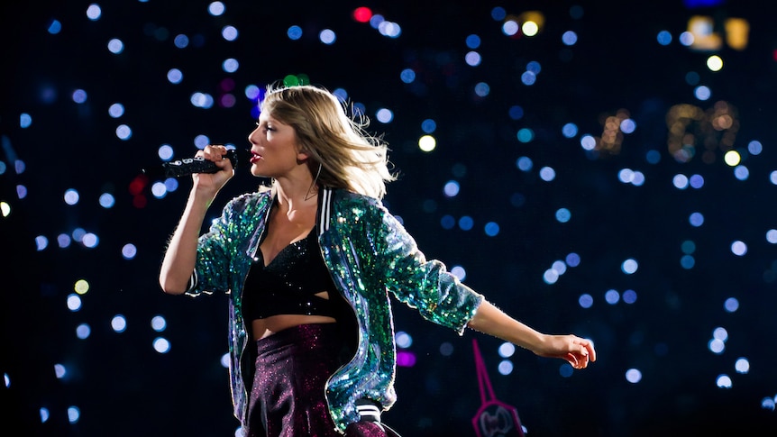 Taylor sings as she waltz on stage in a green glittery jacket and short purple cheerleader skirt.