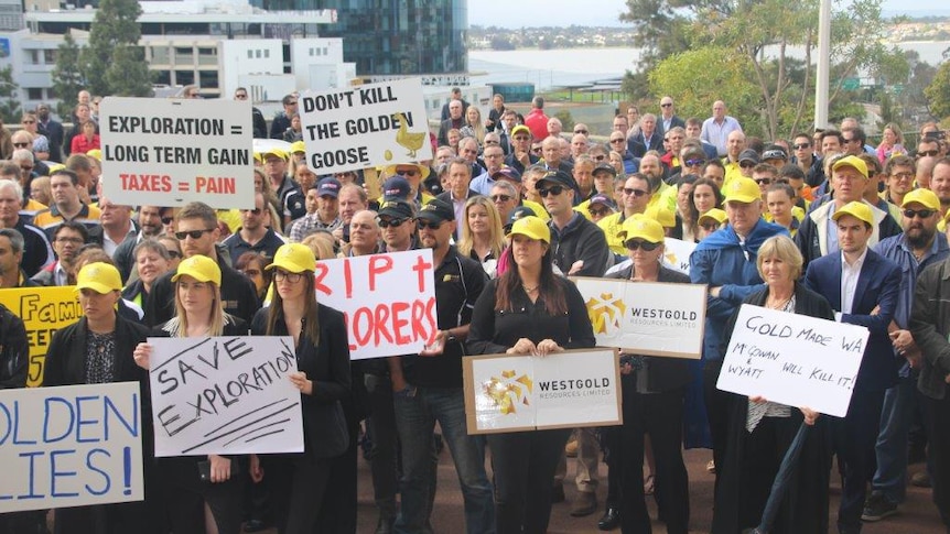 A wide shot showing dozens of protesters holding placards and wearing yellow hats outside Parliament House in Perth.