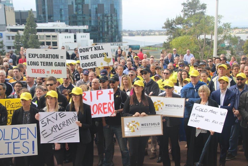 A wide shot showing dozens of protesters holding placards and wearing yellow hats outside Parliament House in Perth.