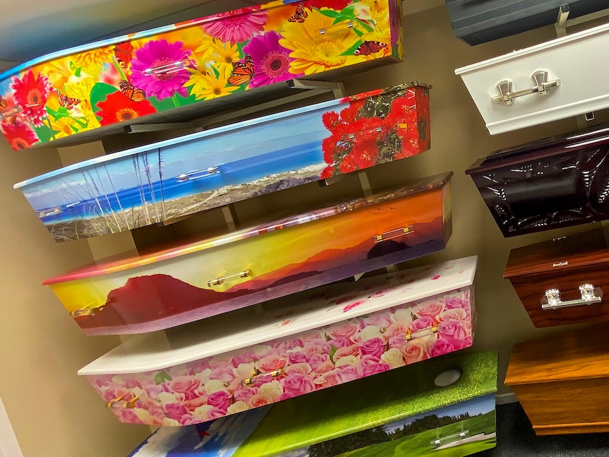 A range of colourful coffins are mounted on a wall. Some are floral, others with a beach scene