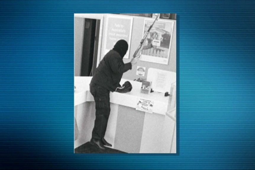 A black-and-white photo of a person leaning over a bank counter with a rifle in their hand