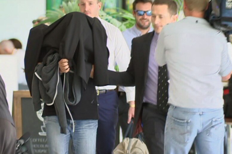 A Malaysian national is escorted by police through the Perth domestic airport.