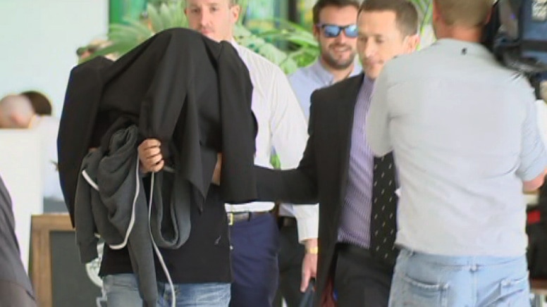 A Malaysian national is escorted by police through the Perth domestic airport.