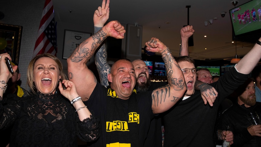 A man in a black shirt and Tigers scraf pumps his arms in the air.