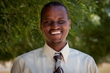 A man of African background, wearing a shirt and tie, smiles for the camera.