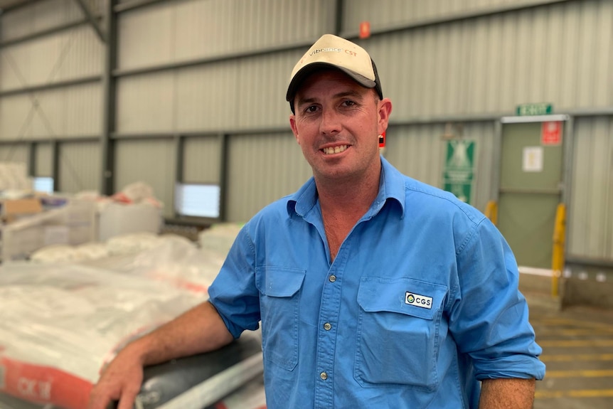 A man in cap and blue shirt stands in a shed