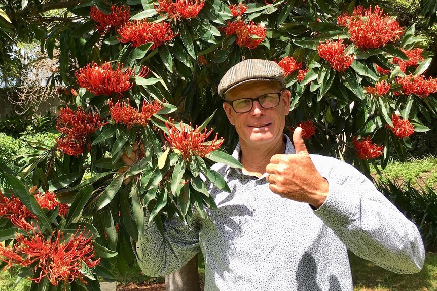 A man gives a thumbs up holding a red flowering tree branch. 