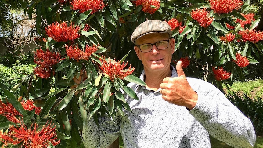 A man gives a thumbs up holding a red flowering tree branch. 