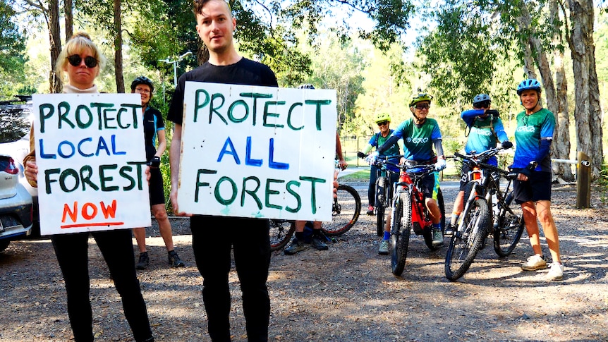two people stand with signs in front of bike riders at Ferny Forest 