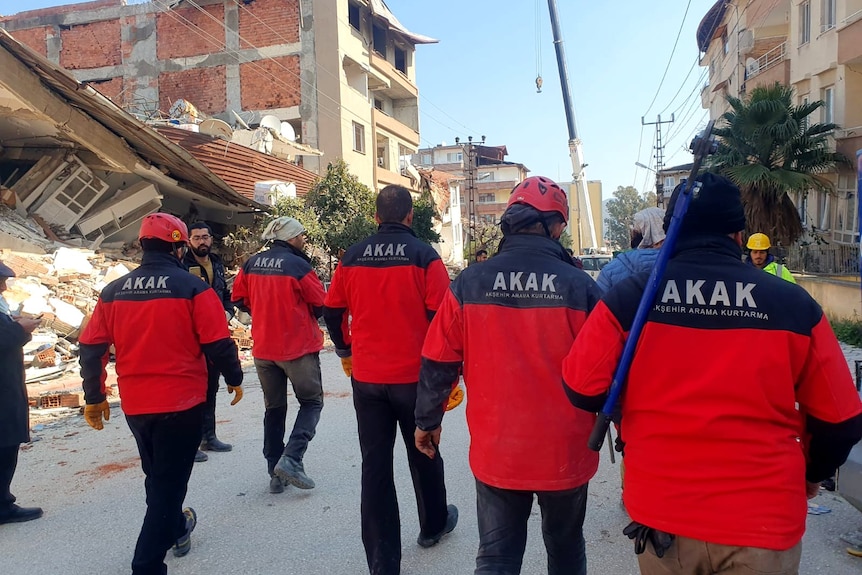 The AKAK rescue team walk along a damaged street in jackets displaying the group's name.