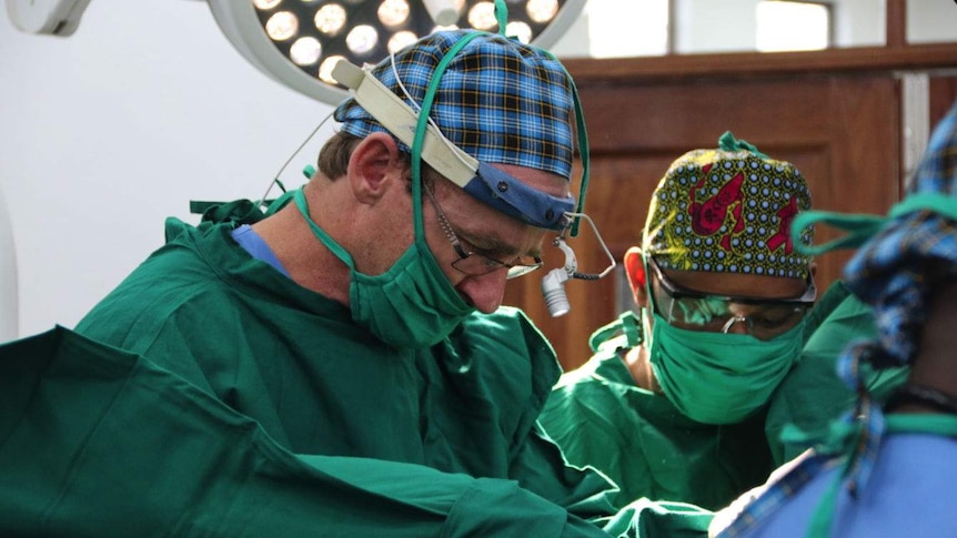 Doctors wearing masks and bandannas operating on a patient.