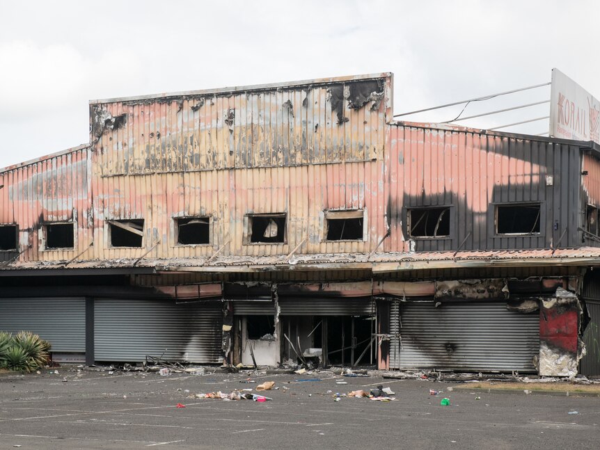 A burnt-out building sits with debris in front of it and burn marks on its exterior