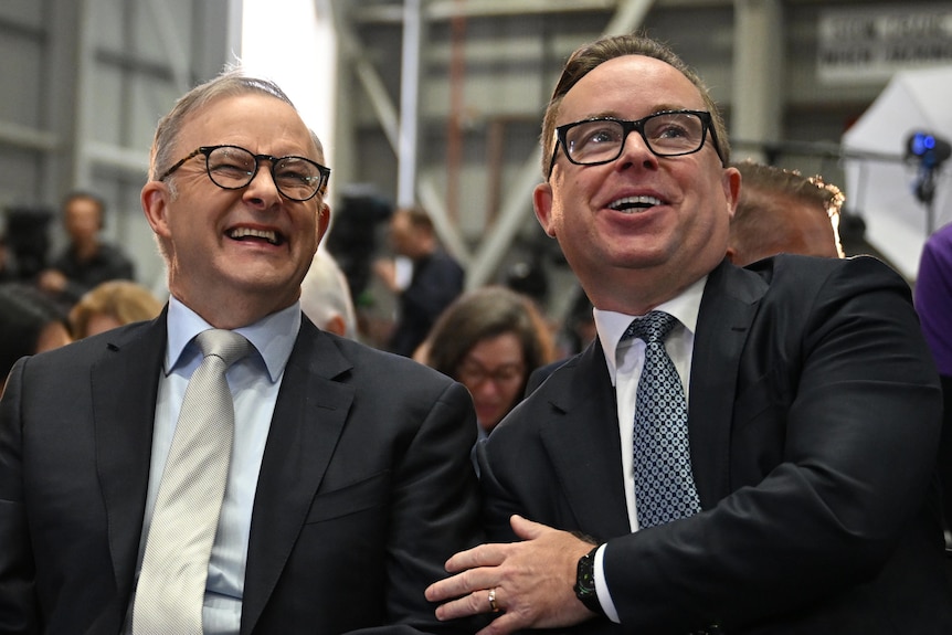 Alan Joyce touches Anthony Albanese as they sit together at an unveiling in a Qantas facility. Adam Goodes is also pictured