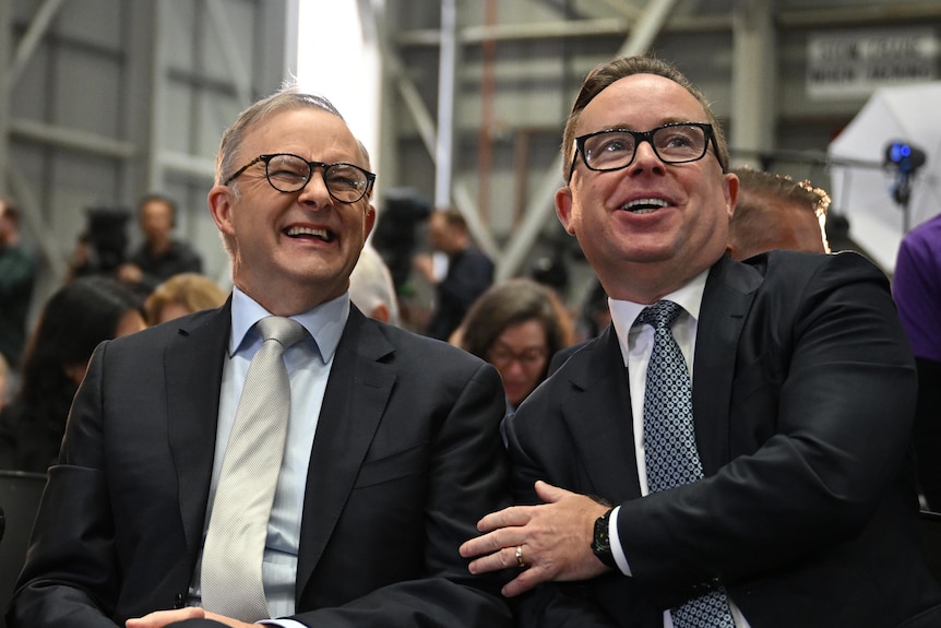 Alan Joyce touches Anthony Albanese as they sit together at an unveiling in a Qantas facility. Adam Goodes is also pictured