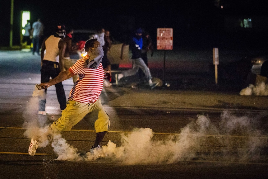 A protester picks up a tear gas canister to throw back towards police as demonstrations continue over Michael Brown's shooting.
