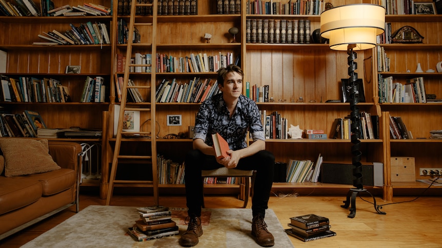 Man sitting on chair in front of book shelf with lamp on
