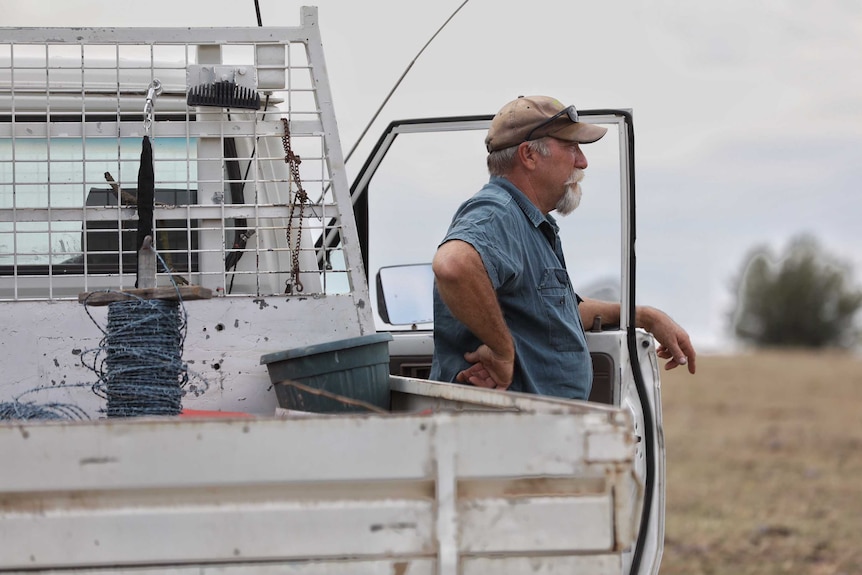 A man looks off into the distance while leaning on a ute.