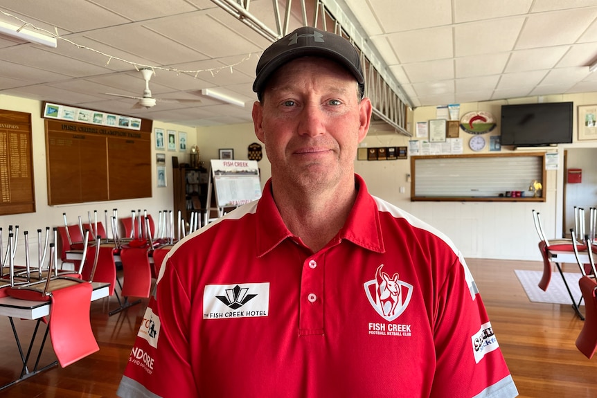 A man in a red-and-white shirt stands at a bowls club.