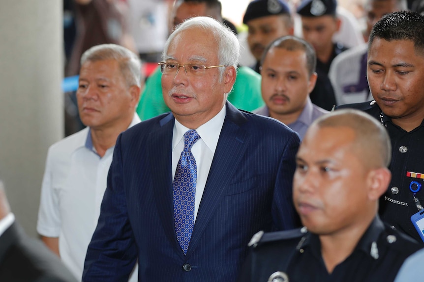 Former Malaysian Prime Minister Najib Razak wearing a blue suit and tie walks into a Kuala Lumpur courtroom.
