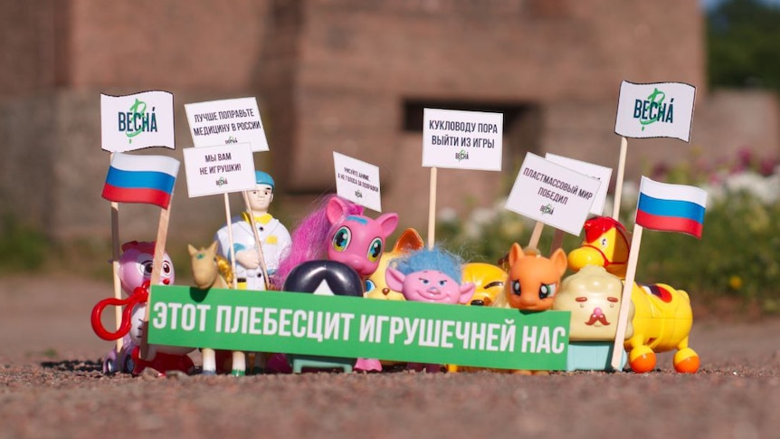 A group of small toys sit behind a green banner with flags beside them.