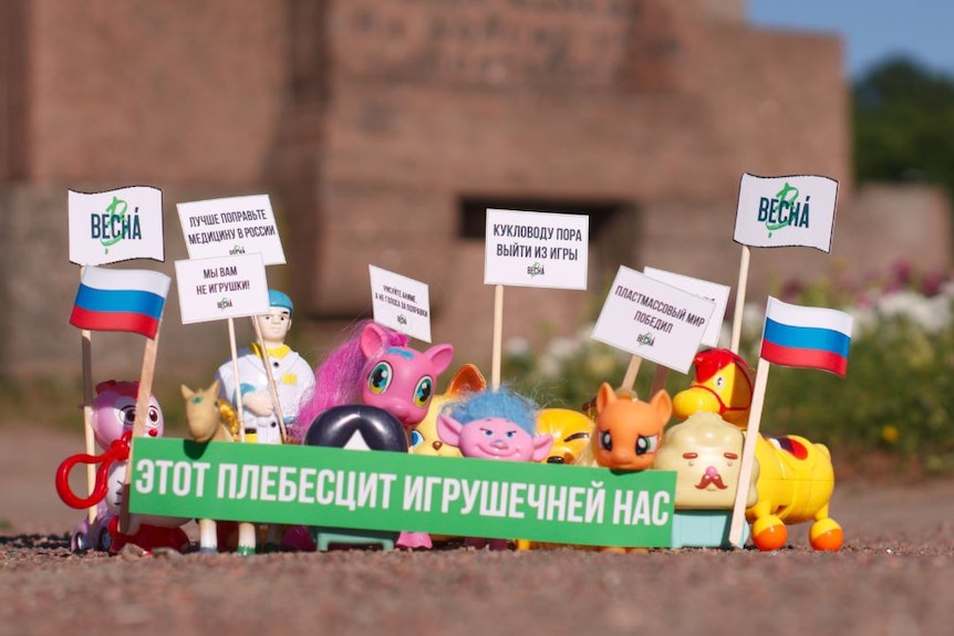 A group of small toys sit behind a green banner with flags beside them.