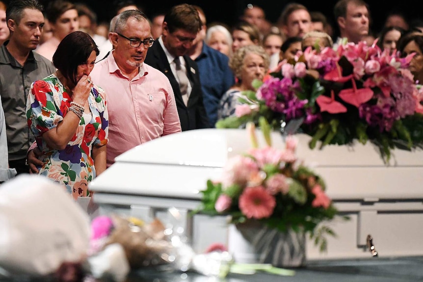 A man and woman in tears as a white coffin passes them by at a funeral