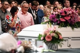 A man and woman in tears as a white coffin passes them by at a funeral