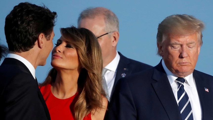 Melania Trump, wearing a red dress, smiles as she leans in to kiss Canadian PM Justin Trudeau on the cheek.